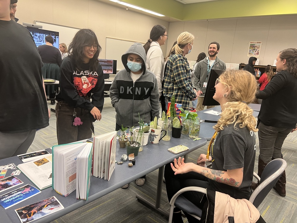 students and science teacher looking at and talking about plants and rock projects that are displayed for the winter showcase in the media centerfor 
