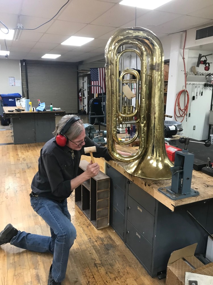 Dr. Steven Prescott repairs a tuba on his work bench. 